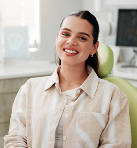 Woman in collared shirt sitting in dental chair and smiling