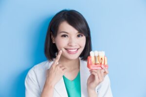 Dentist pointing to her smile while holding dental implant model.